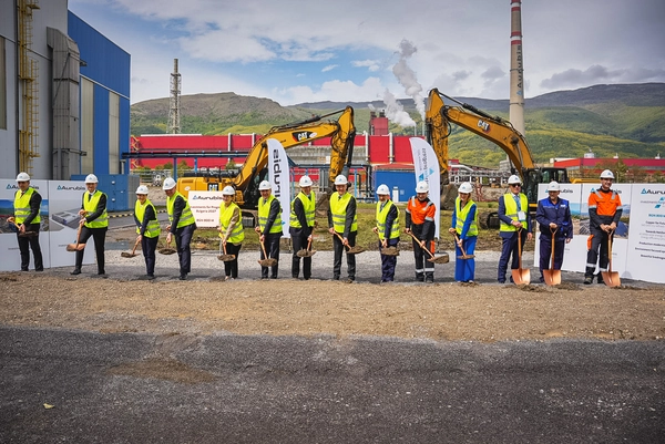 Foto: Aurubis: Viele Menschen mit Helm und Neon-Veste stehen in einer Reihe auf einer Baustelle mit jeweils einer Schaufel in der Hand