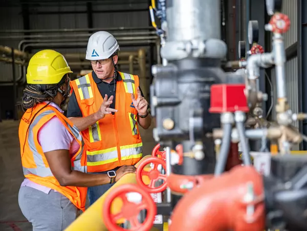 Foto: Aurubis: Drei Arbeiter in Sicherheitskleidung besprechen sich vor einem grossen Industriegeraet