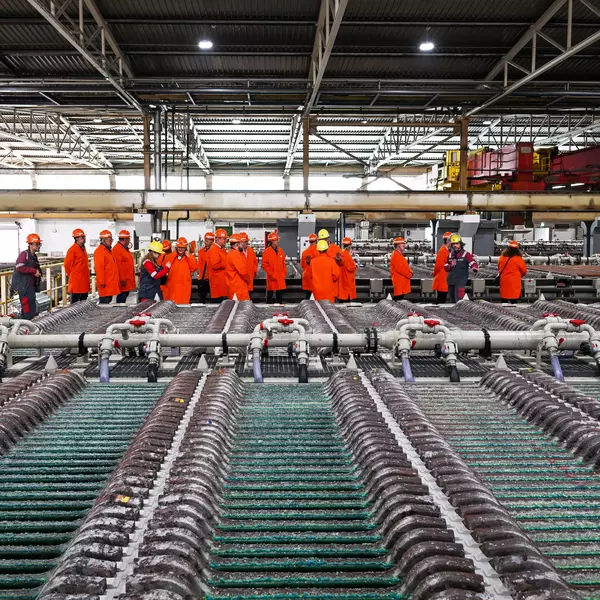 Foto: Aurubis: Mehrere Menschen mit roten Helmen und Jacken stehen in einer Halle vor einer großen Maschine