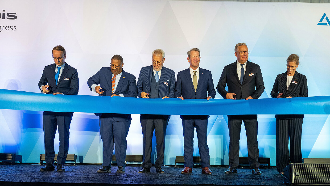 Foto: Aurubis: Mehrere Männer in Anzug schneiden ein blaues festliches Band durch