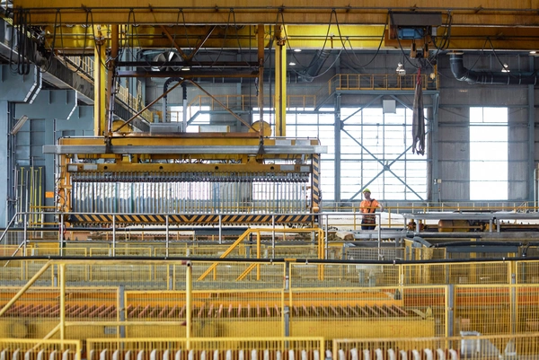 Foto: Aurubis: Eine grosse Metallmaschine in einer Halle die an der Decke befestigt ist, gelbe Gerueste befinden sich darunter 